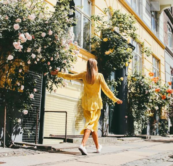 A girl in a yellow dress walks down a rose-lined Copenhagen street