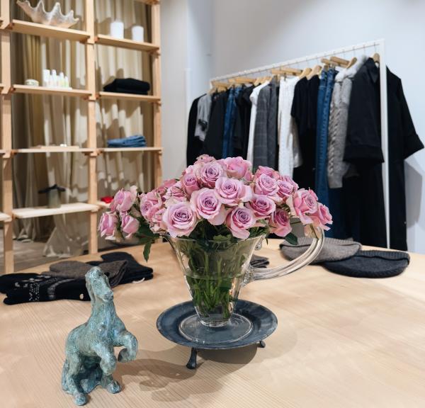 A rack of clothes behind a table with a vase of pink roses