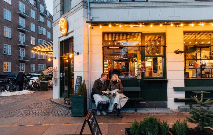 Et par sitter på en benk utenfor en kafe i København på vinteren